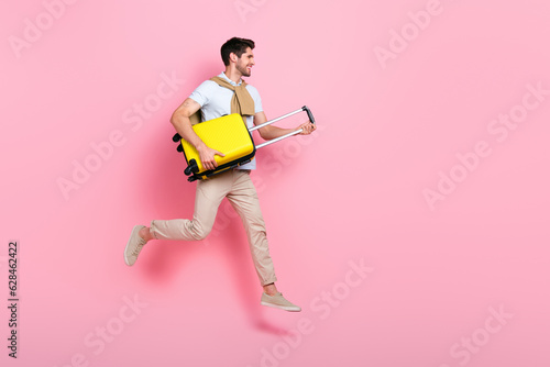 Full body profile photo of carefree nice person hands hold suitcase jump look empty space isolated on pink color background