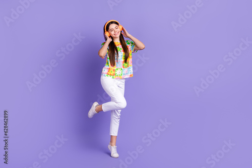 Full size photo of good mood person wear stylish t-shirt white pants touch headphones enjoy playlist isolated on purple color background
