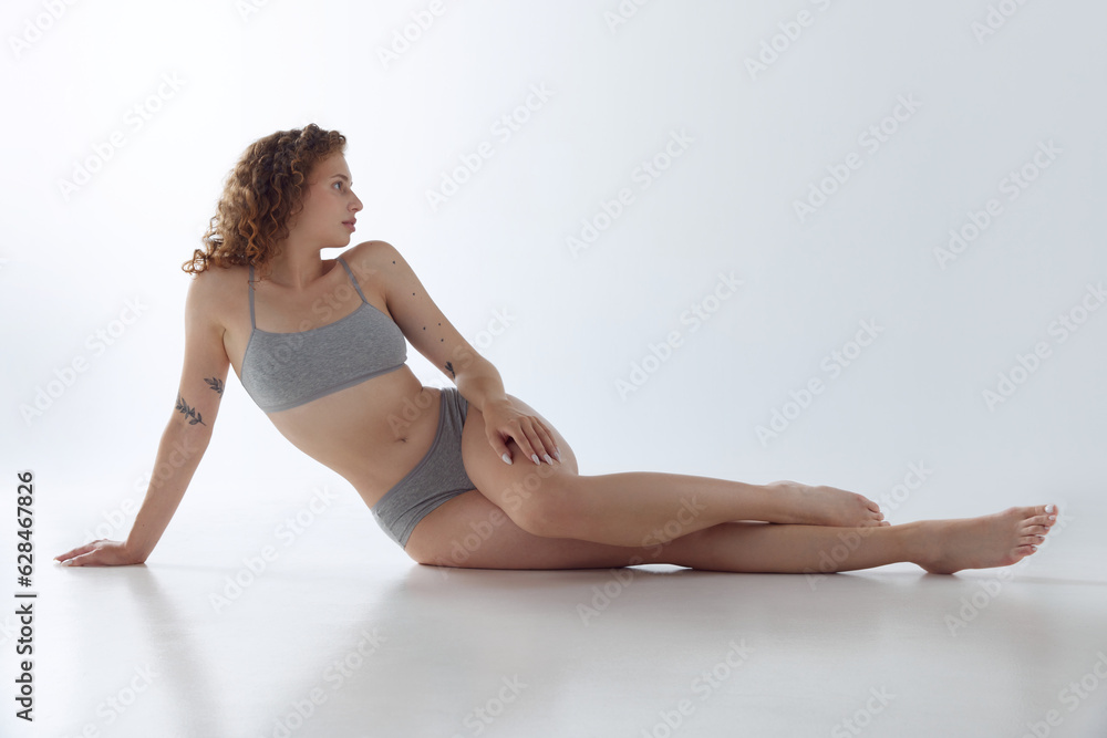 Beautiful young girl with fit, slim figure posing on floor in underwear against studio background. Body care. Beautiful young girl with fit, slim figure posing on floor in underwear against studio background. Body care.