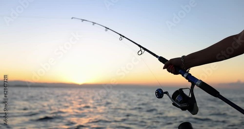 Hands of fisherman holds spinning rod with reel on background of sea. Hobby fishing and tourist photo
