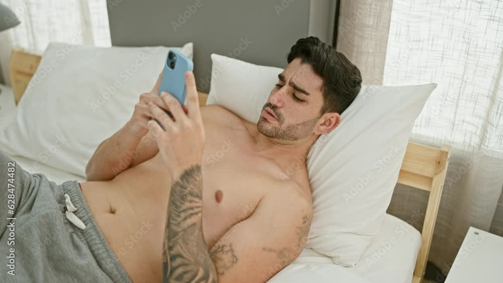 Young hispanic man using smartphone lying on bed at bedroom Young hispanic man using smartphone lying on bed at bedroom