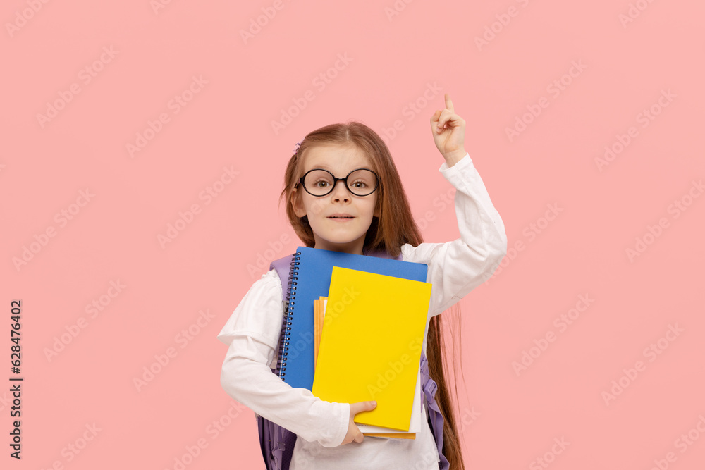 Portrait of a schoolgirl with textbooks and a backpack on a pink background points up. Back to school Portrait of a schoolgirl with textbooks and a backpack on a pink background points up. Back to school
