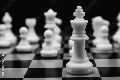 Focus on white chess king with all white chess pieces behind on a chessboard