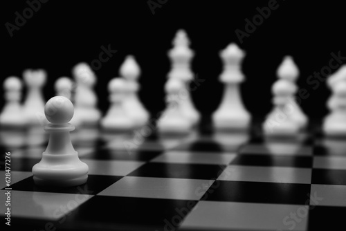 white chess pawn in focus and chess pieces on the black background