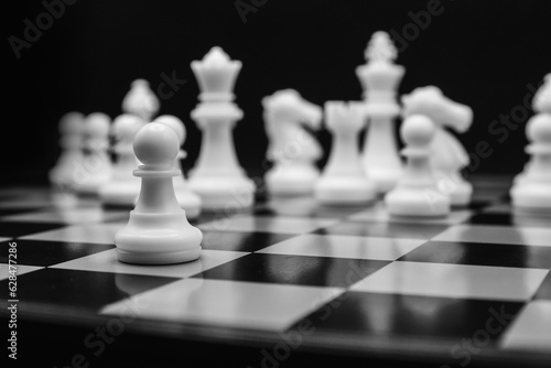 white chess pawn in focus and chess pieces on the black background