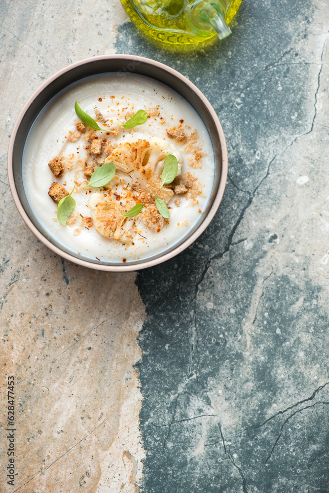 Bowl of cauliflower cream-soup on a beige and grey granite background, vertical shot with copy space, top view Bowl of cauliflower cream-soup on a beige and grey granite background, vertical shot with copy space, top view