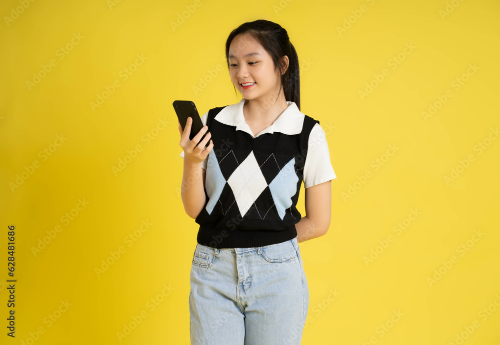 Portrait of a beautiful asian girl using phone on a yellow background Portrait of a beautiful asian girl using phone on a yellow background