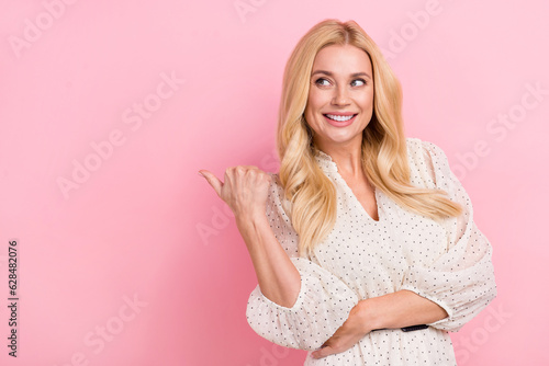 Photo portrait of attractive blonde woman finger point interested empty space wear trendy white clothes isolated on pink color background