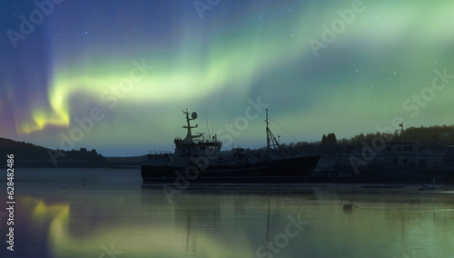 Northern lights in the sky over the city of Tromso, in northern Norway, above the harbor ships during a winter night - Tromso, Norway