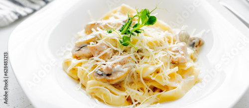 Italian pasta fettuccine alfredo with chicken, mushrooms and sause on plate on light stone table. Closeup.