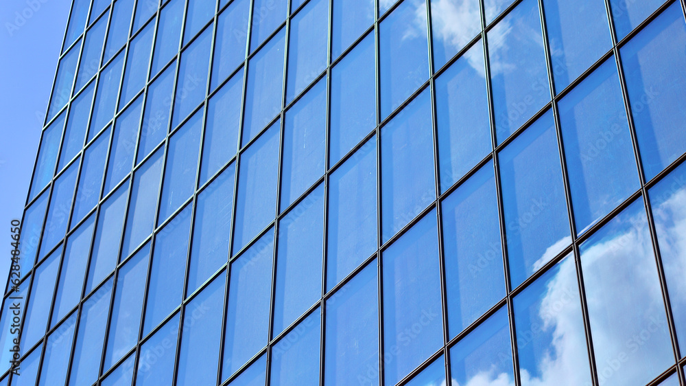 Structural glass wall reflecting blue sky. Abstract modern architecture fragment. Glass building with transparent facade of the building and blue sky. Contemporary architectural background. Structural glass wall reflecting blue sky. Abstract modern architecture fragment. Glass building with transparent facade of the building and blue sky. Contemporary architectural background.