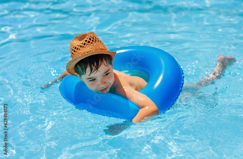 cute boy with beach sunny hat swimming in pool with inflatable ring tube.smiling adorable boy clean brite blu water summer vacation photo