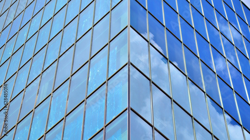Structural glass wall reflecting blue sky. Abstract modern architecture fragment. Glass building with transparent facade of the building and blue sky. Contemporary architectural background.