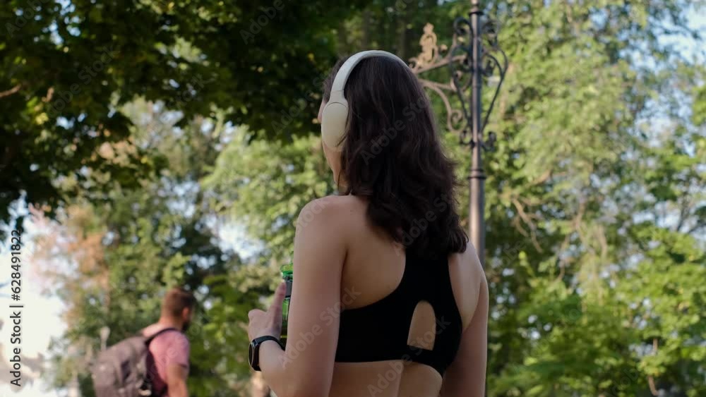 Young happy girl doing yoga in the park, listening to music with headphones, sitting in lotus position, meditating, enjoying being alone in balance, drinking water, running or jogging in a public park Young happy girl doing yoga in the park, listening to music with headphones, sitting in lotus position, meditating, enjoying being alone in balance, drinking water, running or jogging in a public park