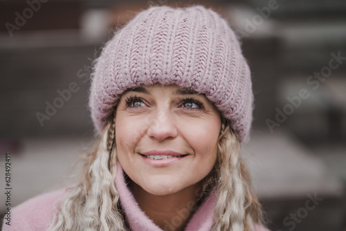 Fashionable mature woman in a pink knitted beanie hat and stylish coat outdoors in a cafe in autumn. Middle aged woman positive and smiling with pigtails in the city. Blur and selective focus