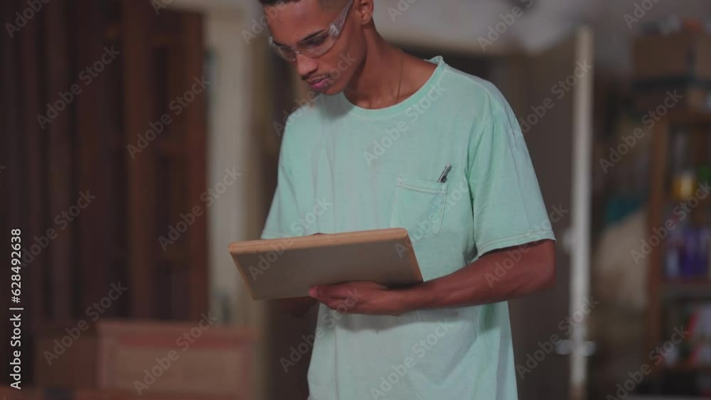 One young black Brazilian carpenter working at carpentry workshop, trimming piece of wood with machine. Concentrated apprentice engaged with work One young black Brazilian carpenter working at carpentry workshop, trimming piece of wood with machine. Concentrated apprentice engaged with work