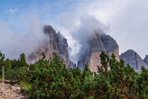 Stunning view of the mountains covered with thick clouds. Picturesque landscape with high sharp rocks, green grass, majestic trees, cloudy sky in the Dolomites, Italy. Adventure and hiking © Alexander
