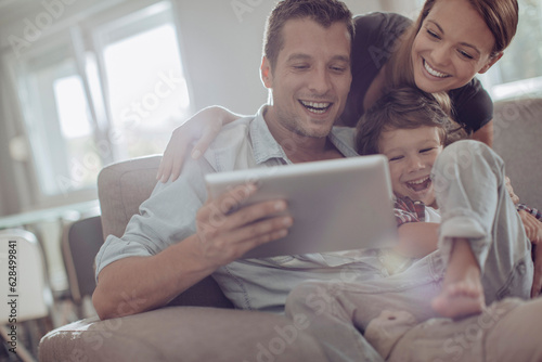 Young family using a digital tablet while sitting on the couch in the living room