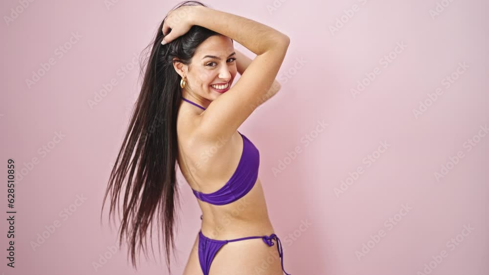 Young beautiful hispanic woman tourist wearing bikini combing hair with hands over isolated pink background Young beautiful hispanic woman tourist wearing bikini combing hair with hands over isolated pink background