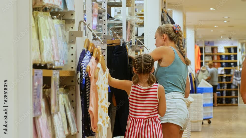 Happy mother and little daughter choose looking for clothes in shopping mall.Mother and daughter shopper customer is looking and buying casual clothes in clothing store.Concept shopping clothes store Happy mother and little daughter choose looking for clothes in shopping mall.Mother and daughter shopper customer is looking and buying casual clothes in clothing store.Concept shopping clothes store