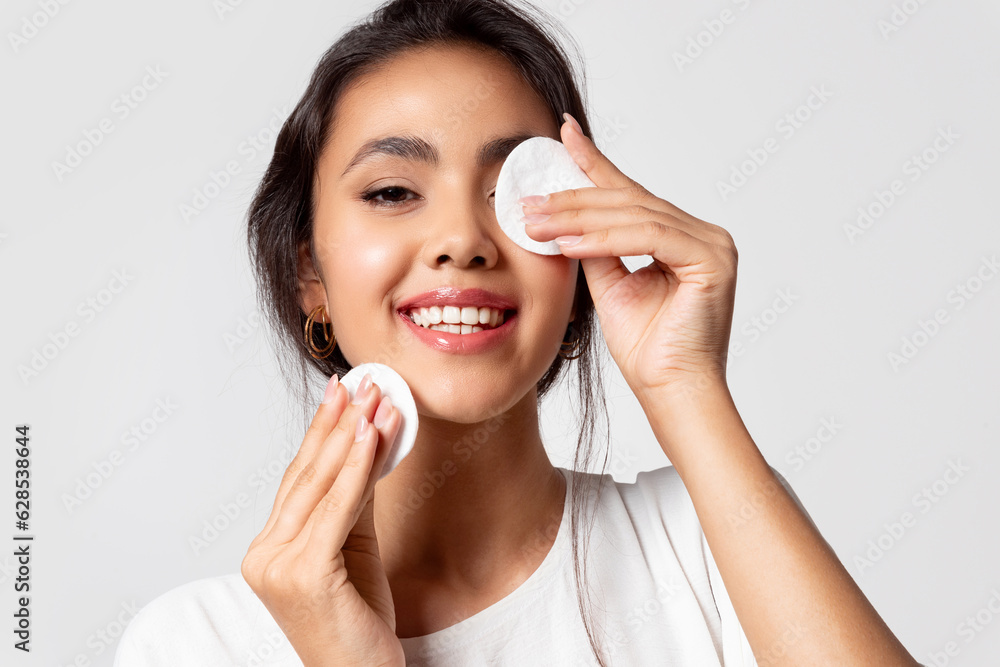 Modern asian woman removing makeup from face using cotton pads, apply cleansing cosmetics products to make skin clear Modern asian woman removing makeup from face using cotton pads, apply cleansing cosmetics products to make skin clear