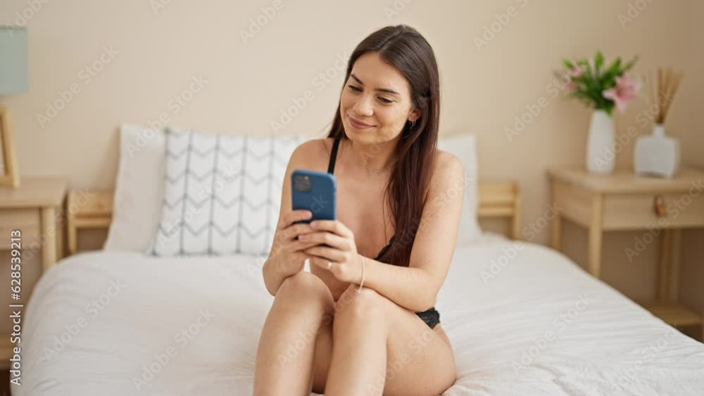 Young beautiful hispanic woman wearing lingerie using smartphone at bedroom Young beautiful hispanic woman wearing lingerie using smartphone at bedroom