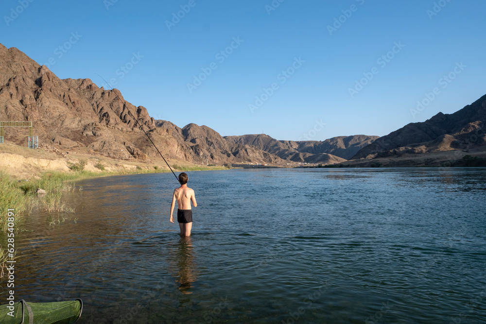 A teenager throws a fishing rod standing in the water. Fisherman on the river