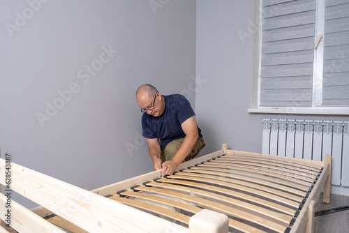 A man is assembling a new wooden bed in the room.