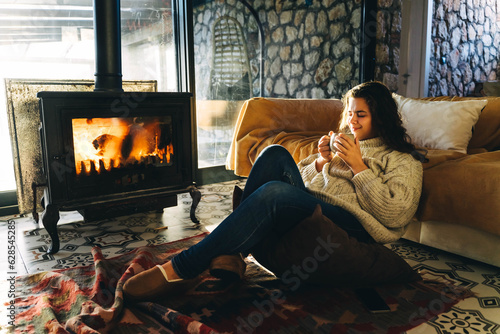Woman in sweater has rest near the fireplace.
