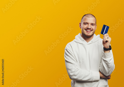 Young handsome man holding credit card isolated on yellow background. Online shopping, e-commerce, internet banking, spending money concept © Davidovici