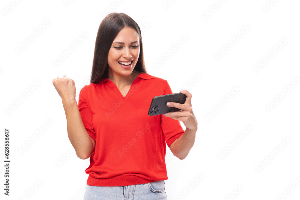 A 30-year-old smiling Caucasian woman with straight dark hair is dressed in a red short-sleeved shirt watching a video on a mobile phone A 30-year-old smiling Caucasian woman with straight dark hair is dressed in a red short-sleeved shirt watching a video on a mobile phone