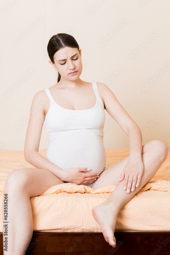 Obraz premium Pretty pregnant woman hands massaging leg sitting on bed