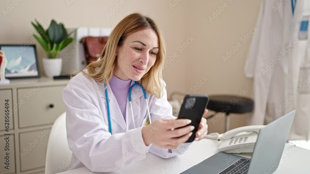 Young beautiful hispanic woman doctor doing video call with smartphone at clinic Young beautiful hispanic woman doctor doing video call with smartphone at clinic