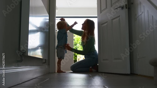 Mother measuring height of young son at home standing against wall in kitchen silhouetted against bright window - shot in slow motion photo