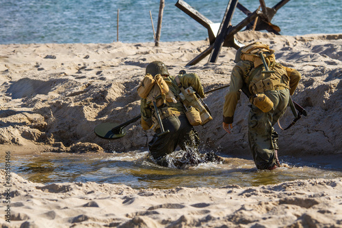 Historical reconstruction. An American infantry soldiers from the World War II fighting on the beach. View from the back.