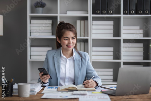 Portrait of young business woman with sitting in office in front of her laptop and talking on mobile phone hand at office