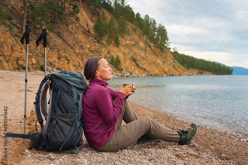 Hiking tourism adventure. Backpacker woman resting after hiking looking at beautiful view. Hiker girl lady tourist with backpack sitting near lake. Hiker woman enjoy hike tourism active vacation
