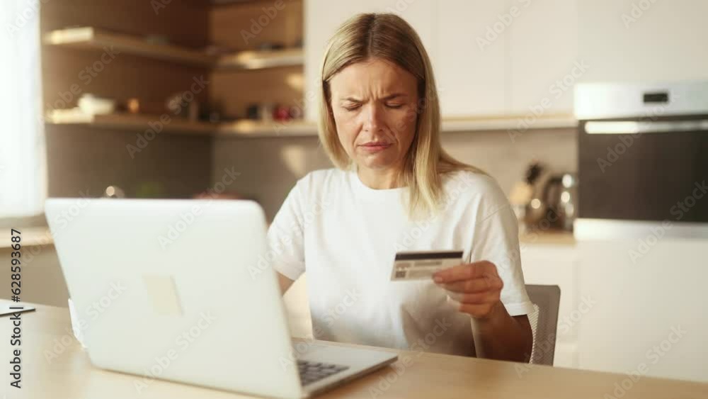 Confused blond woman with credit card thoughtfully pondering on screen while has problem with online order payment error or blocked bank account doing shopping at internet on laptop at light home Confused blond woman with credit card thoughtfully pondering on screen while has problem with online order payment error or blocked bank account doing shopping at internet on laptop at light home