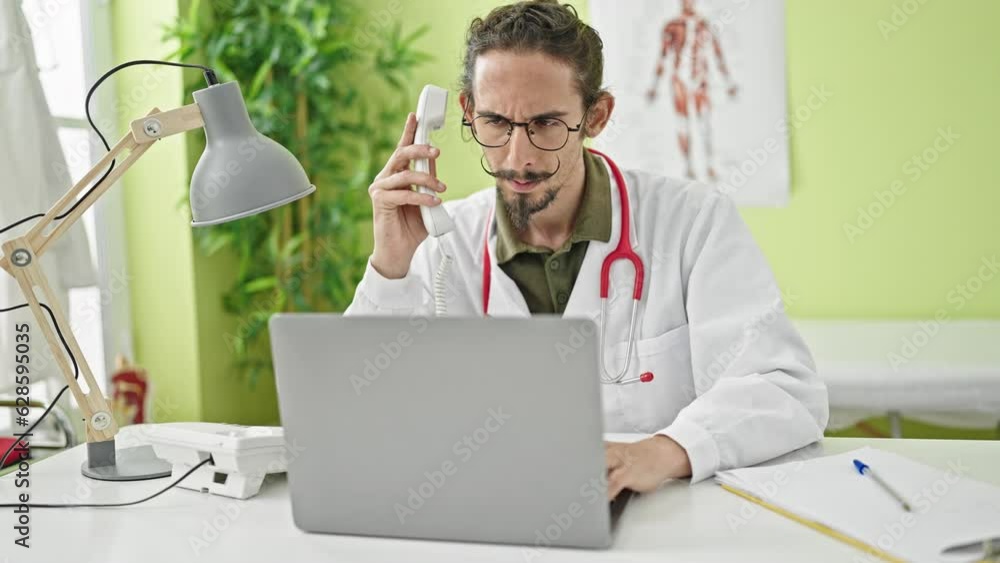 Young hispanic man doctor using laptop talking on telephone at clinic Young hispanic man doctor using laptop talking on telephone at clinic