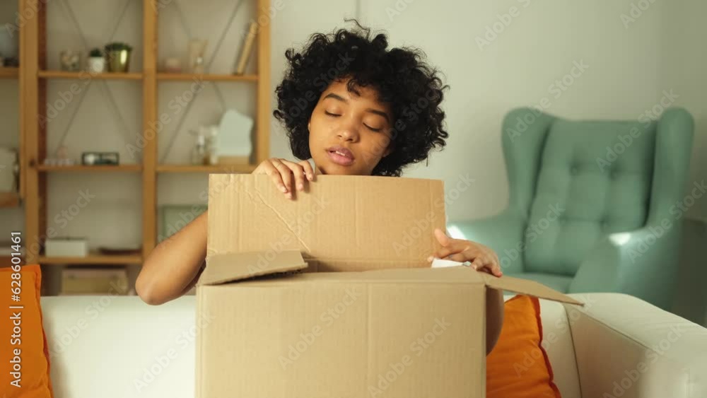 African girl unpacking delivery looking in box. Happy woman opening carton box. Female getting parcel looking at delivered goods items. Satisfied client positive feedback quick express deliver African girl unpacking delivery looking in box. Happy woman opening carton box. Female getting parcel looking at delivered goods items. Satisfied client positive feedback quick express deliver