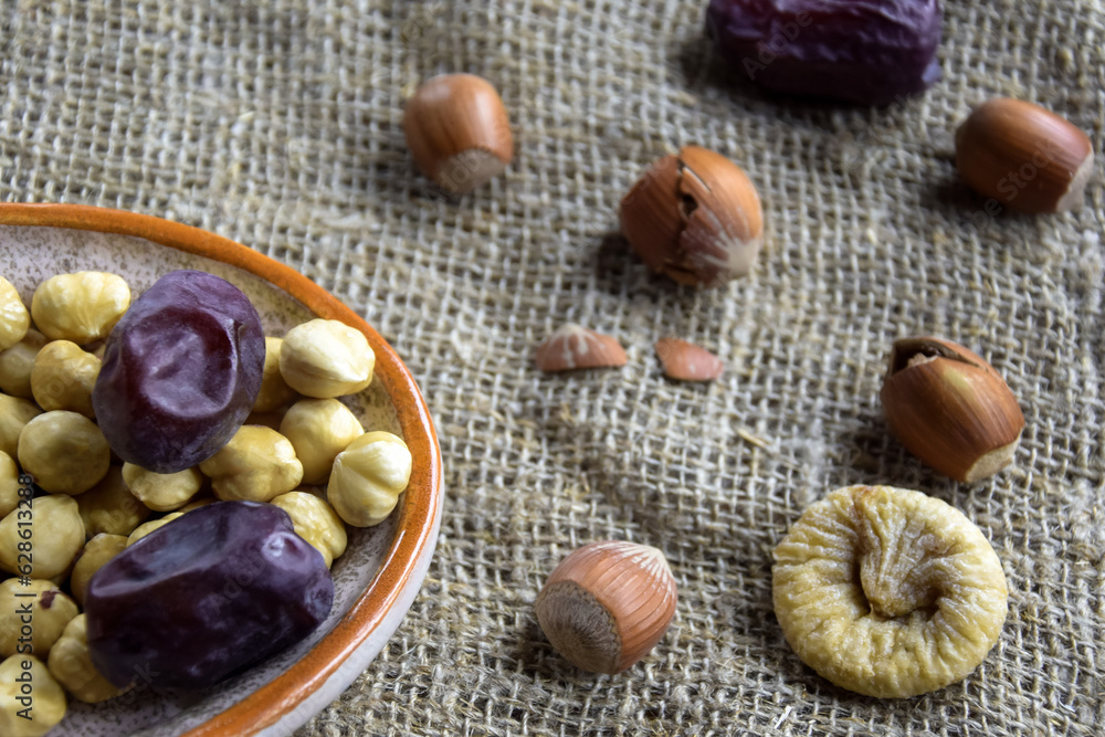 Filbert kernels, sweet dates, figs and hazelnuts in a shell on burlap background. Healthy nutrition, diet food, dried fruits and nuts. Close-up. Shallow depth of field. Selective focus.