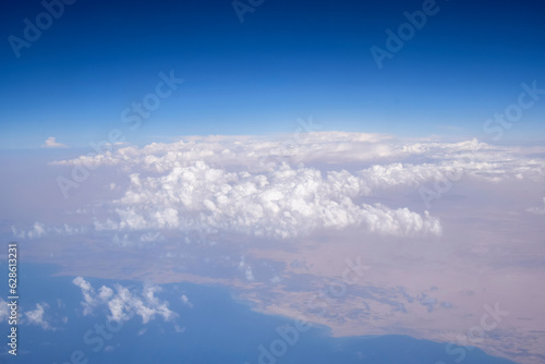 Cloudy sky. Beautiful sky with white fluffy cumulus clouds, natural abstract background. View from plane to sea and mountain landscape. Selective focus.