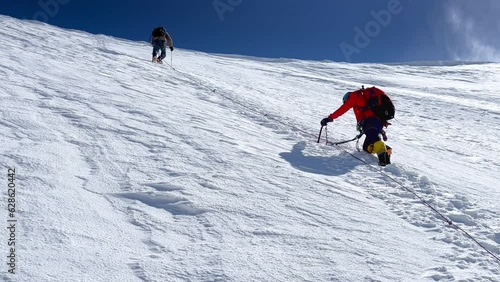 Last steps before Kazbek (Kazbegi) summit 5054m rope team dressed mountaineering clothes, boots with crampons ascending steep snowy slope using climbing ice axes. Windy Caucasus mountains 4K footage photo