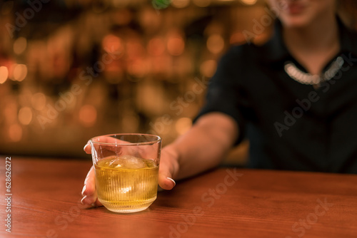 Close-up of a girl bartender putting a cocktail with ice on the bar and serving it to a customer 