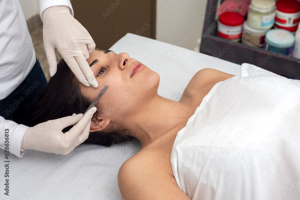 young woman on a table in a beauty center performing a beauty treatment for facial skin with the dermaplaning technique young woman on a table in a beauty center performing a beauty treatment for facial skin with the dermaplaning technique