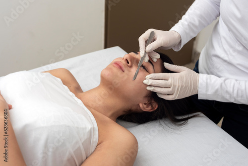 young woman on a table in a beauty center performing a beauty treatment for facial skin with the dermaplaning technique