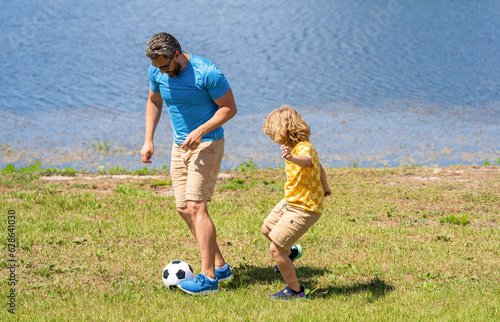 Father and son enjoy a friendly game of football. happy childhood of son playing with father. father and son summer activity. son has bonding time with father outdoor. rewards of fatherhood