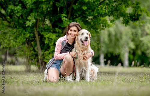 Pretty girl with golden retriever dog sitting at nature. Beautiful young woman hugging purebred pet doggy labrador in park at summer