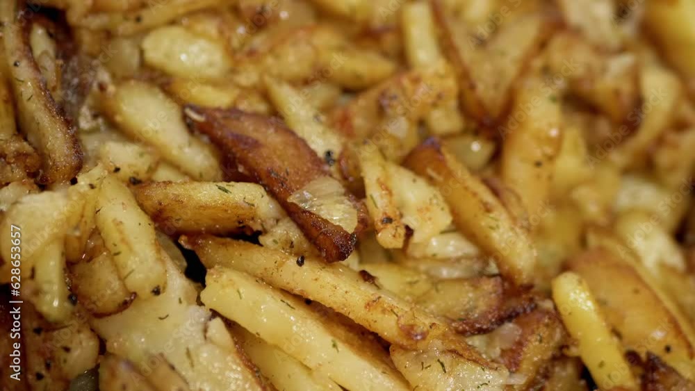 Fried Potatoes with a Golden Crust in a Frying Pan on a Rotating Background. Close up. Texture. Juicy slices of crispy french fries in oil with spices cooked in a home kitchen. Side view. Slow motion. Fried Potatoes with a Golden Crust in a Frying Pan on a Rotating Background. Close up. Texture. Juicy slices of crispy french fries in oil with spices cooked in a home kitchen. Side view. Slow motion.