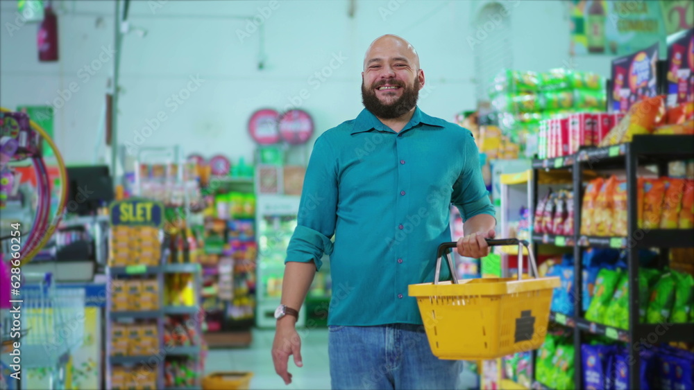Happy Brazilian man standing at Grocery Store holding basket in hand smiling at camera, consumer habits of South American supermarket shopper